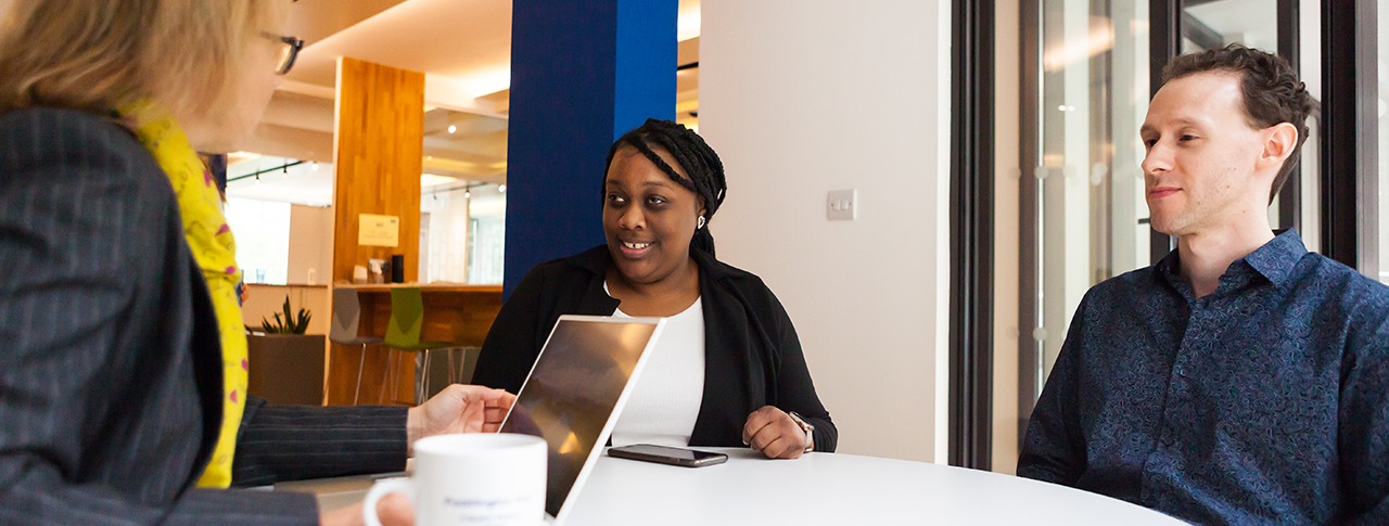 Three people in business attire sat around roundtable