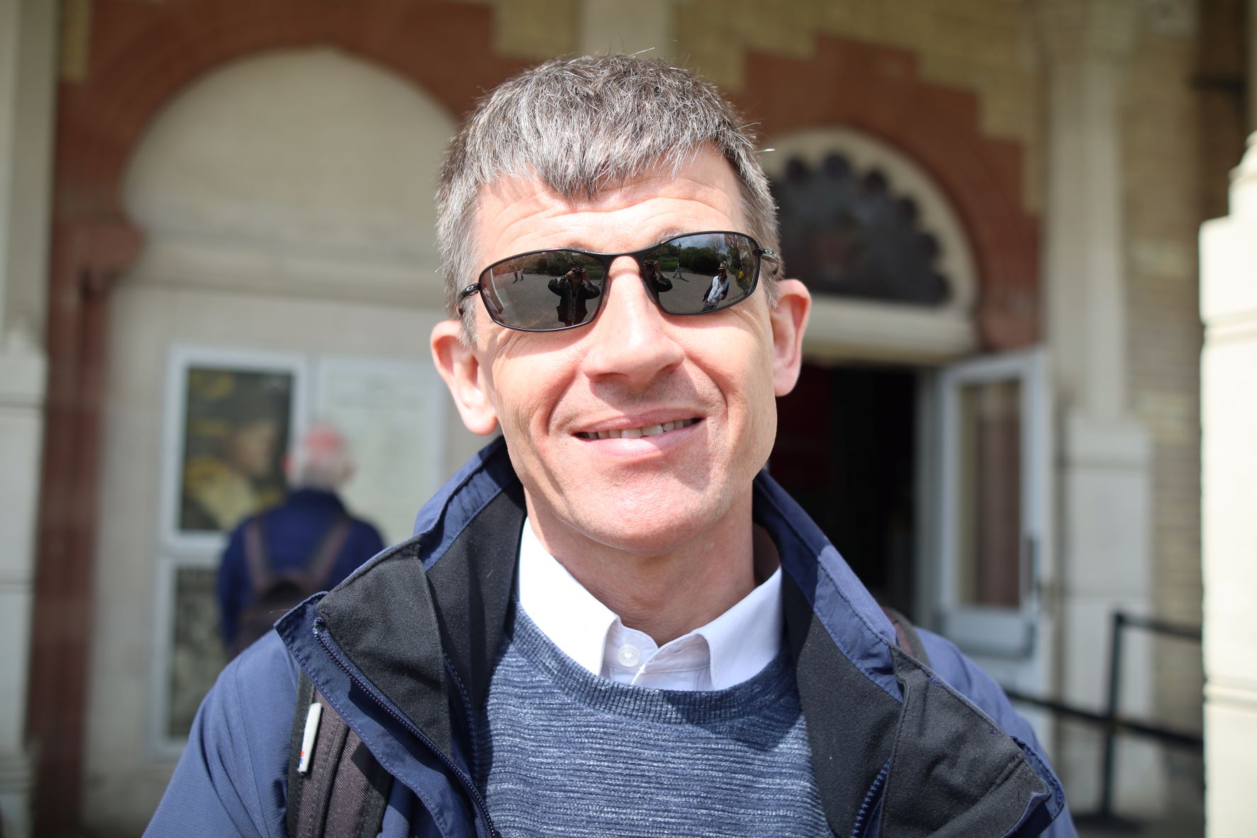 Headshot of Dave Smith, Engagement Manager for South East England. The photo is taken outside a railway station. Dave is wearing dark sunglasses, and smiling at the camera.