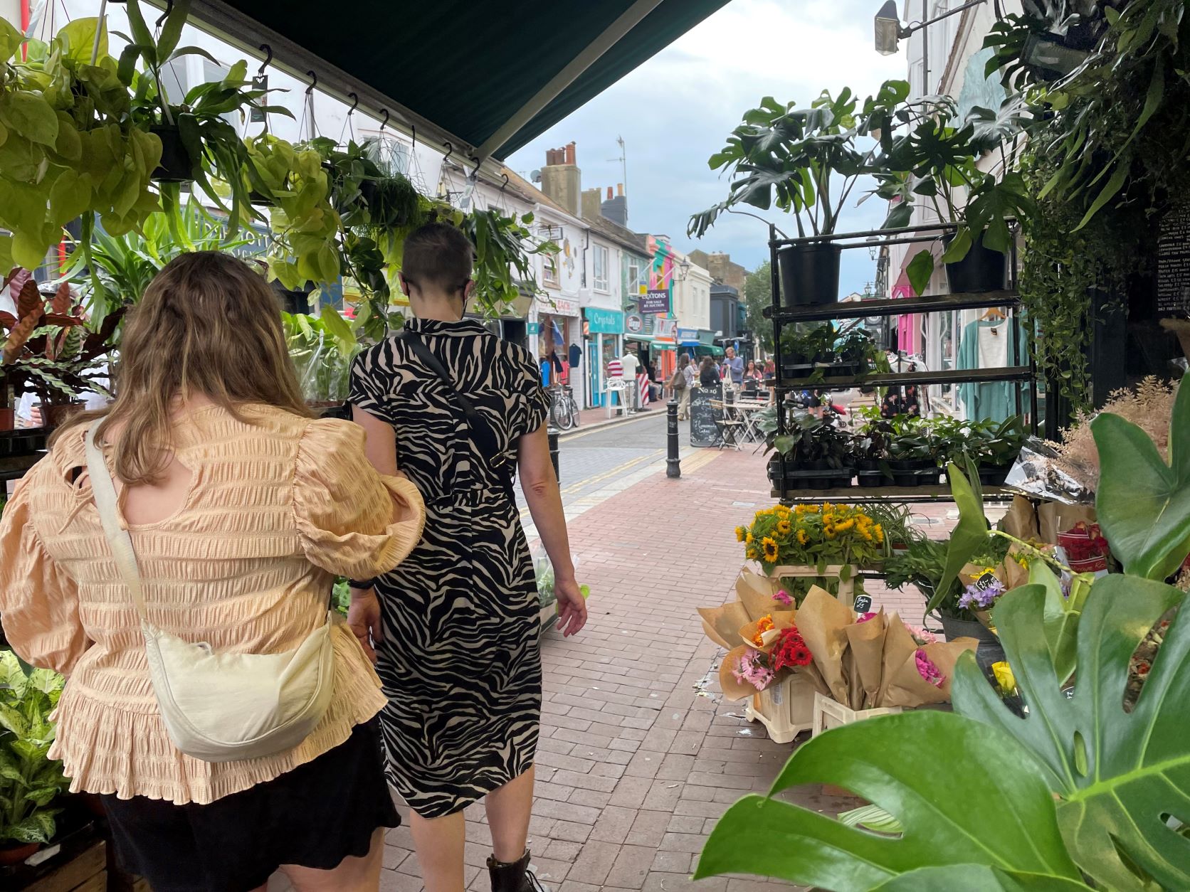 Image taken from behind Cllr Amy Healy who is guiding Cllr Sarah Nield through a narrow walkway, lined with plants and flowers either side.