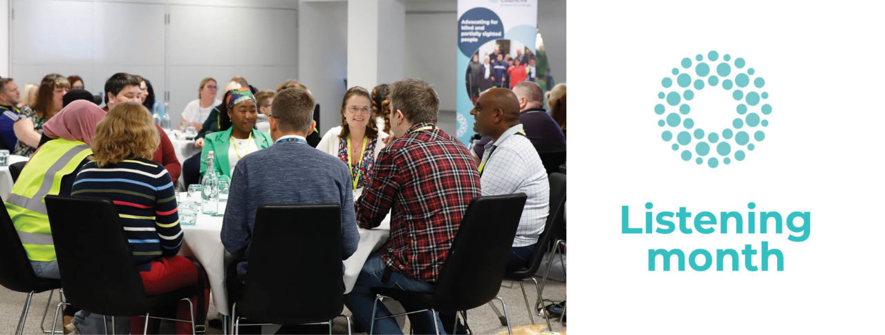 Group of blind and partially sighted Sight Loss Council members are sat around a table discussing key topics. A Sight Loss Council banner is in the background.