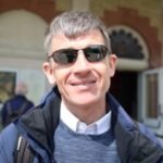 Headshot of Dave Smith. Dave is wearing sunglasses, a grey jumper and white shirt while smiling at the camera.