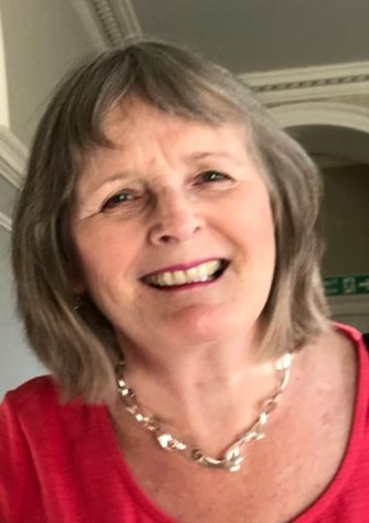 Headshot of Josie Clarke. Josie is wearing a red top and a chunky silver necklace. She has shoulder-length hair. She is smiling at the camera.