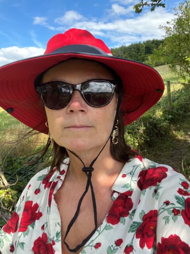 Headshot of London SLC member, Vicky Blencowe. Vicky is outside and wearing a red sunhat, sunglasses and white and red flowery shirt.