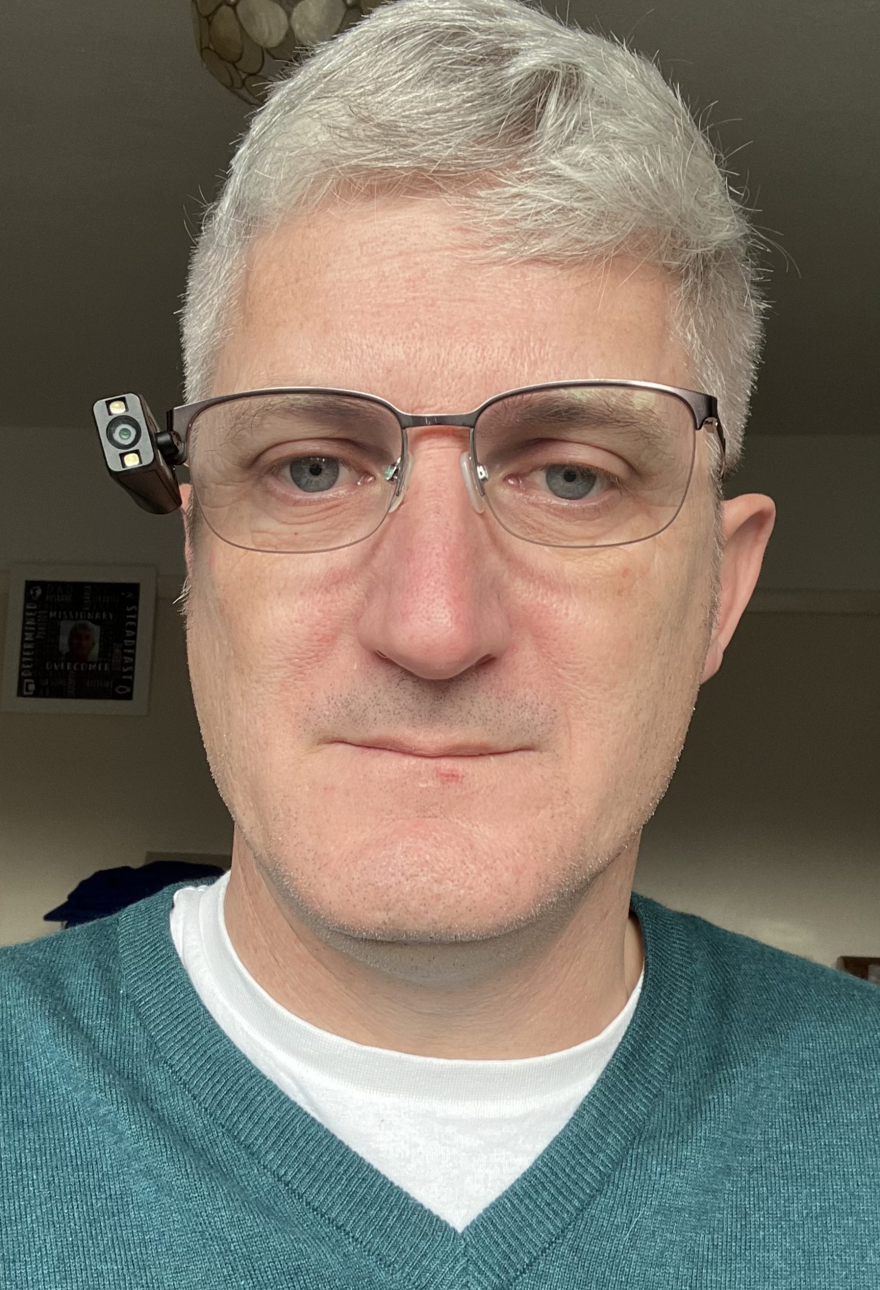 Headshot of Clinton Corrin, West Sussex SLC member. Clinton has short grey hair, wearing glasses, and a dark green V-neck jumper.