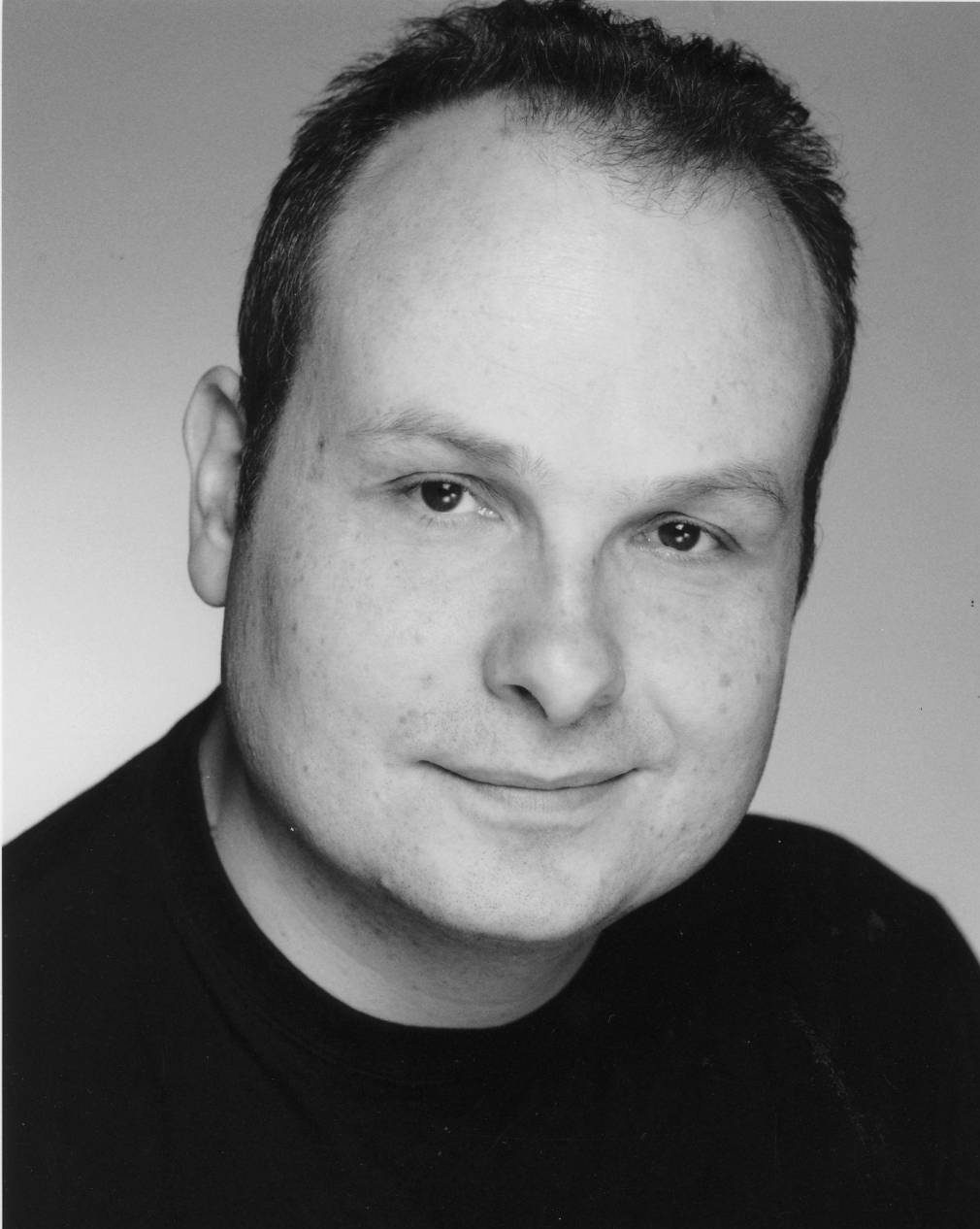 Black and white headshot of Liam O'Carroll. His head is turned slightly to the side and he is smiling.