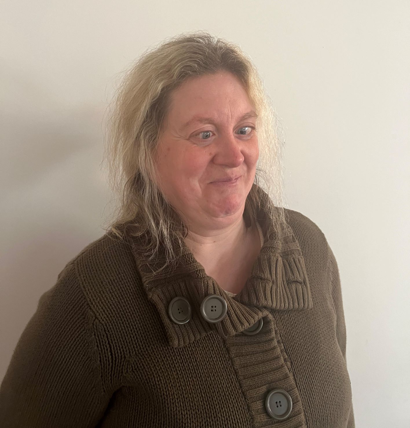 York SLC member, Verity Peat. Verity is standing at an angle against a cream wall. Her head is tilted towards the camera, and she is smiling.