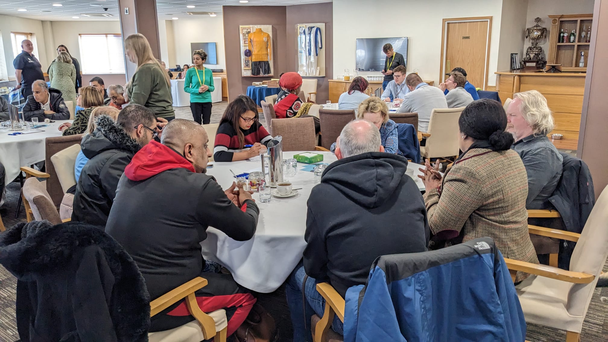 Table discussions with blind and partially sighted delegates, Sight Loss Council members and Jamie Reilly (Vulnerabilities Team, University Hospitals Birmingham). Delegates are sat around circular tables in a large room.