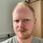 James Langley headshot. James has fair hair and a beard and is wearing a grey t-shirt. He is facing the camera, smiling.