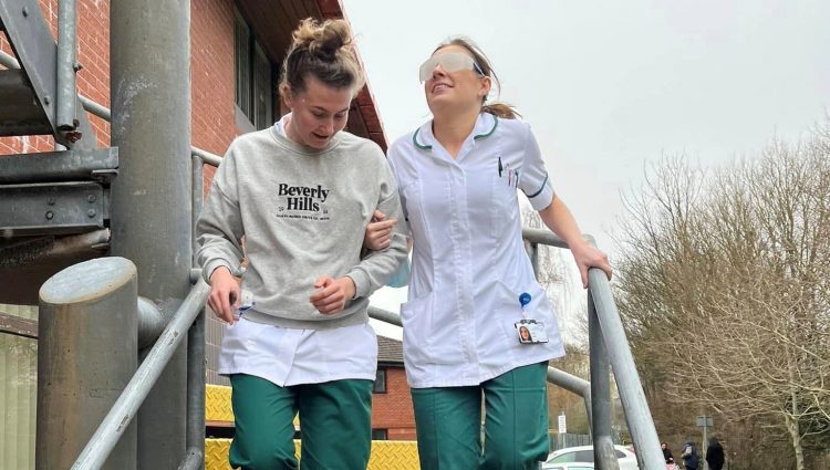 Two nurses from Southport Hospital, walking down a staircase as part of a vision awareness session. One nurse is being guided, whilst wearing simulation spectacles.