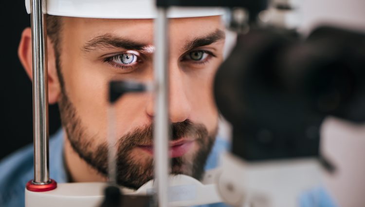 Close up image of a man having an eye examination. His chin is resting on the slit lamp, and a light is shining on his eye.