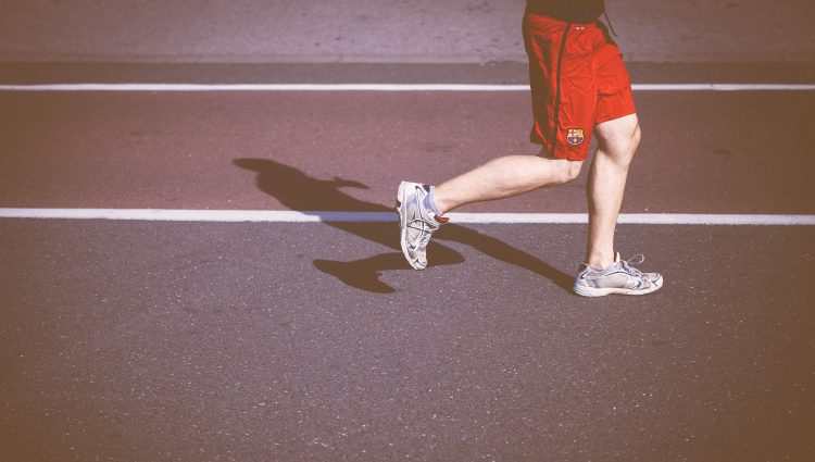 Image shows a man running on an athletics track from the waist down. He is wearing red shorts and white trainers.