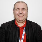 Headshot of Emmanuel Beck, London Sight Loss Council member. Emmanuel is wearing a red polo shirt and black jacket. He is facing the camera, with a big smile on his face,