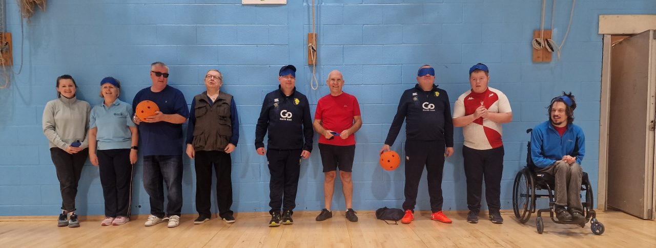 Lets Get Active attendees are standing in a line in the main sports hall, waiting for the Goalball session to start.