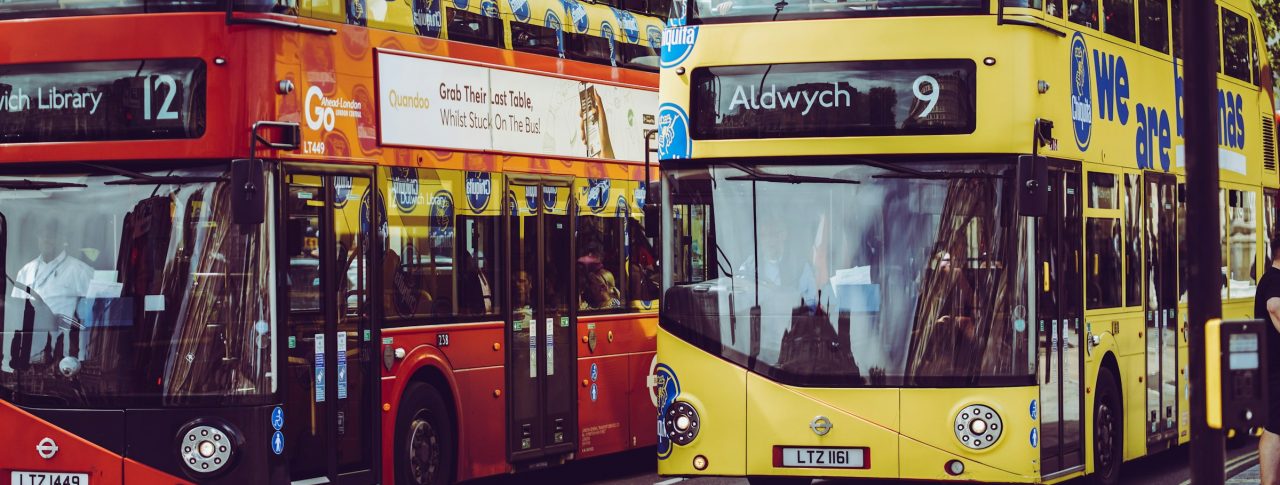 A pair of London buses driving down the road. The one of the right says Aldwych and the number 9 at the front.