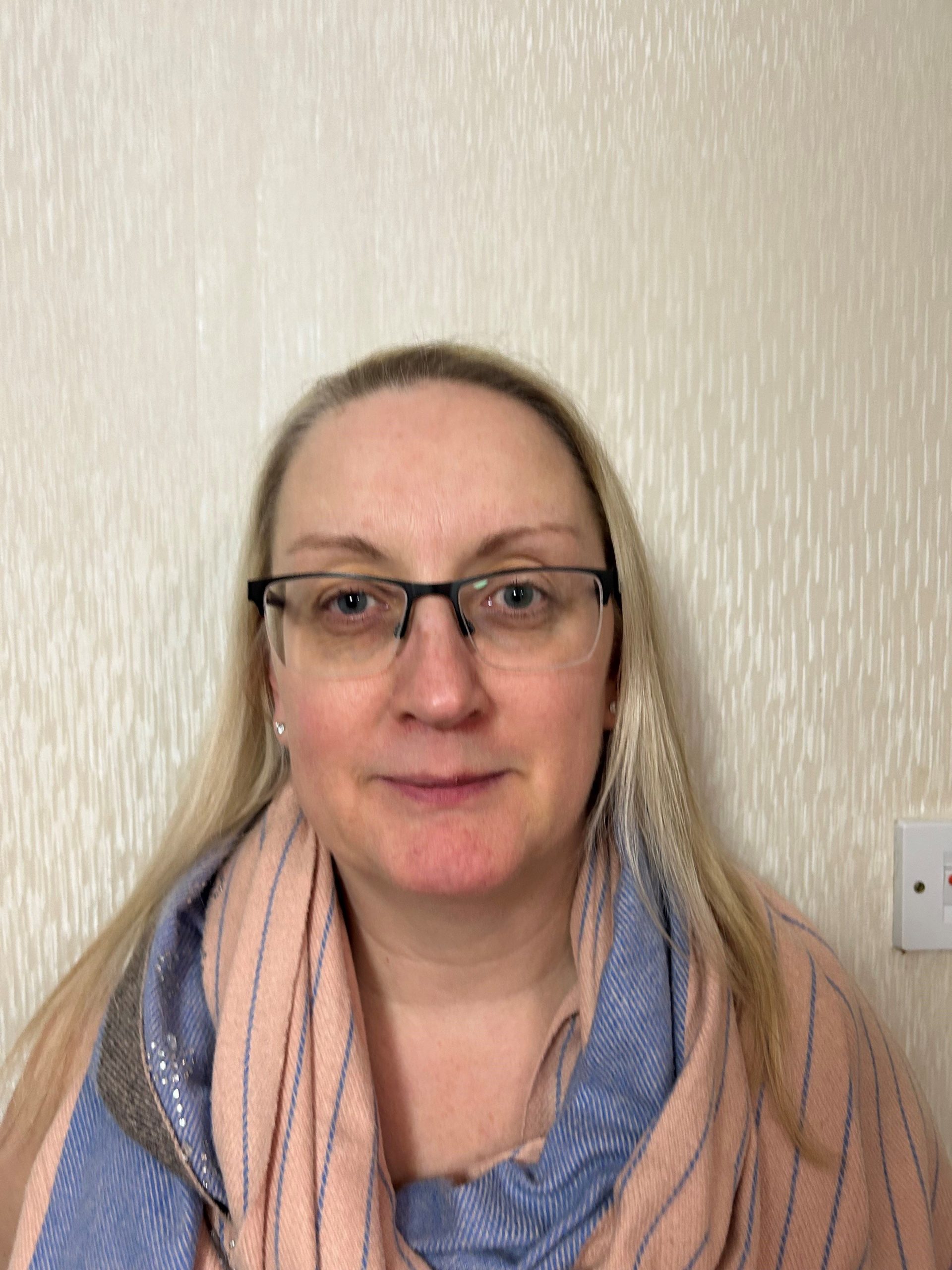 Headshot of Greater Manchester SLC member, Gill Douglas. She is standing against a cream wall, smiling at the camera.