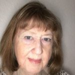 Headshot of Judy Blowe. Judy has short brown and wearing a cream blouse with black polka dots. She is smiling at the camera.