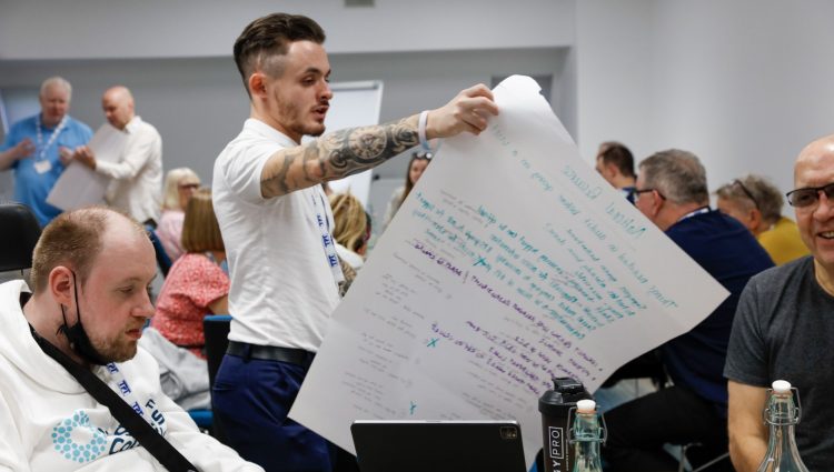 David Parfett, SLC Coordinator for the North West, reading from a large sheet of paper with notes on it at a table of delegates during a session at the SLC conference.