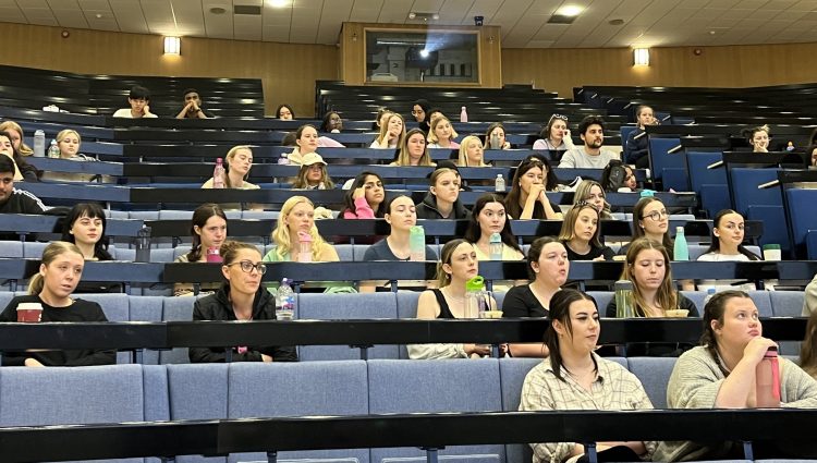 Several rows of Liverpool University healthcare students, sat in the auditorium, looking forwards to the stage.