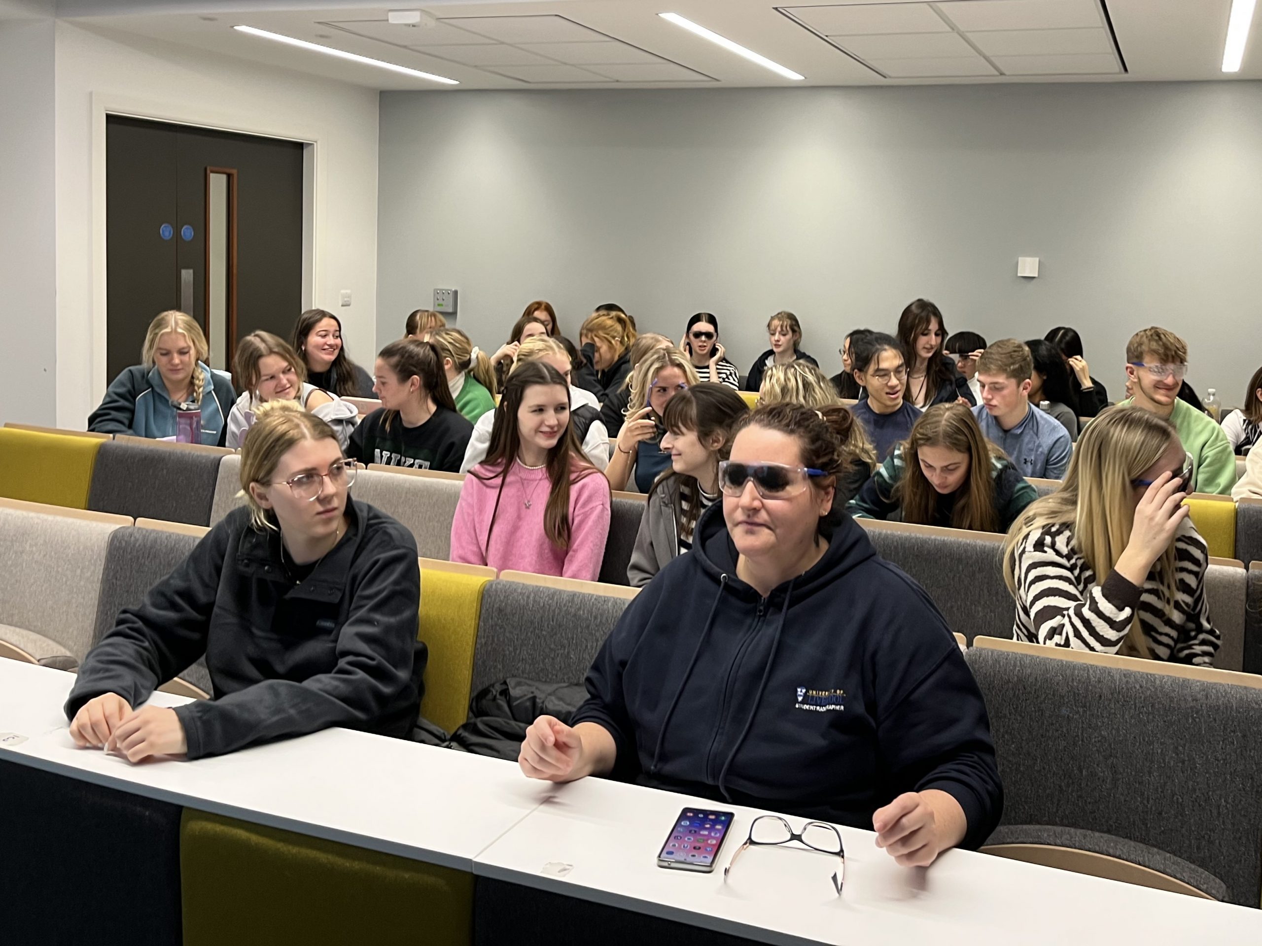 Liverpool University healthcare students sitting at tables, trying on simulation spectacles.