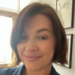 Headshot of Nicki Guy, Senior Engagement Manager for South England. She is standing in a hallway in front of prints on a wall, smiling at the camera.