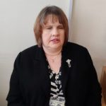 Rebecca Green, South Yorkshire SLC member. Rebecca has chin length brown hair and is wearing a black and white dress and black blazer. She is sitting down, looking towards the camera.