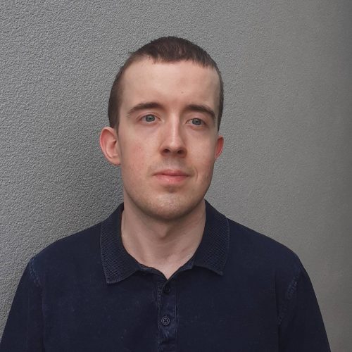 Headshot of Jordan, South East London SLC member. Jordan has short dark hair and is standing against a grey background, smiling at the camera.