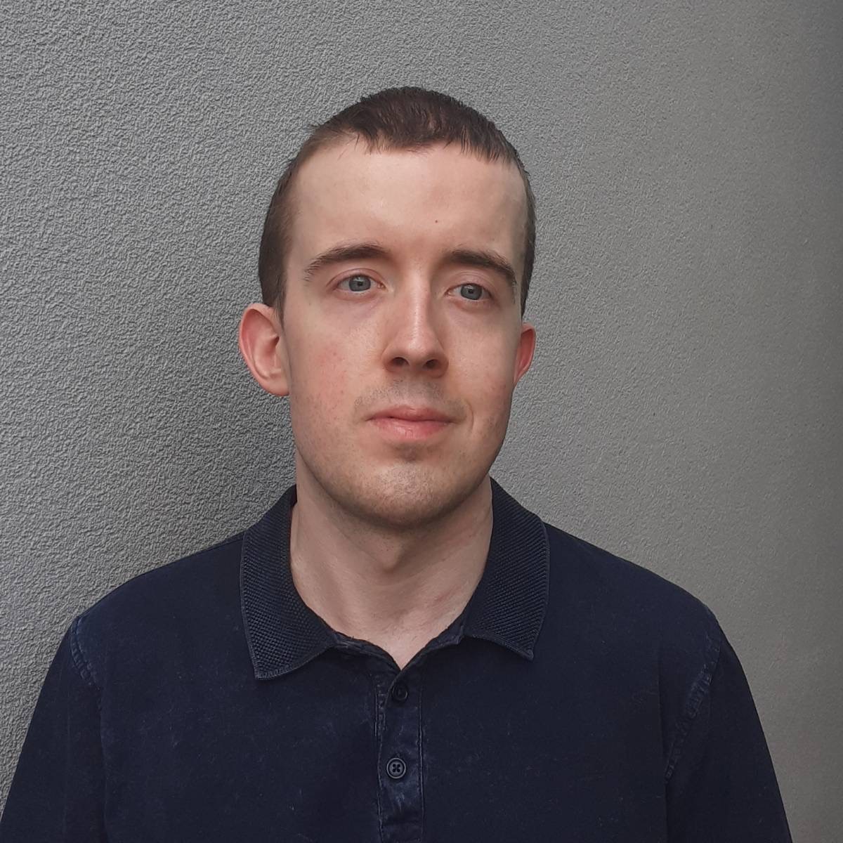 Headshot of Jordan, South East London SLC member. Jordan has short dark hair and is standing against a grey background, smiling at the camera.