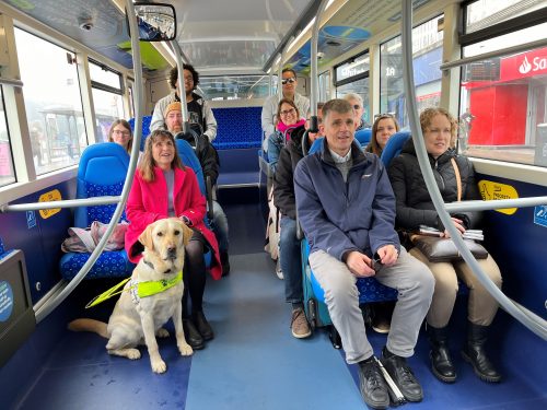Sight Loss Council and Young Voices volunteers, and Thomas Pocklington staff, are sat on a bus creating some of the videos used in the training materials. Two passengers have white canes with them and there is a guide dog sat at the front.