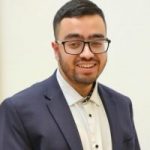 Bilaal Ali headshot. Bilaal is wearing a navy blazer and white shirt and glasses. He is smiling at the camera.