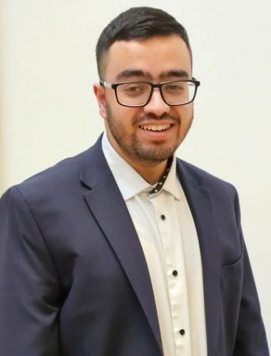 Bilaal Ali headshot. Bilaal is wearing a navy blazer and white shirt and glasses. He is smiling at the camera.