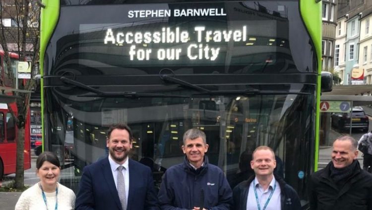 Dave stood with Transport Minister Simon Lightwood, Victoria Garcia, Ed Wills and another outside of Coaster bus at a bus stop. They are stood infront of the bus and smiling a the camera. The green bus says 'Accessible Travel' and the words 'Stephen Barnwell' at the top.