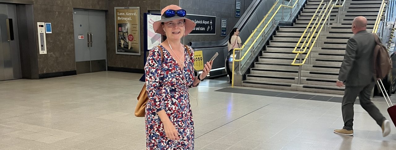 Vicky Blencowe, South West London SLC member, pictured at London Blackfriars train station. She is facing the camera, and holding her smartphone in her hand, whilst on the phone to an AIRA representative.