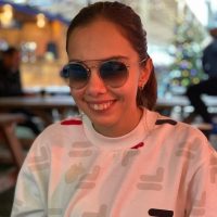 Student Voices volunteer, Zehra, smiling at the camera. She is wearing a white jumper and has her hair tied up in a ponytail.