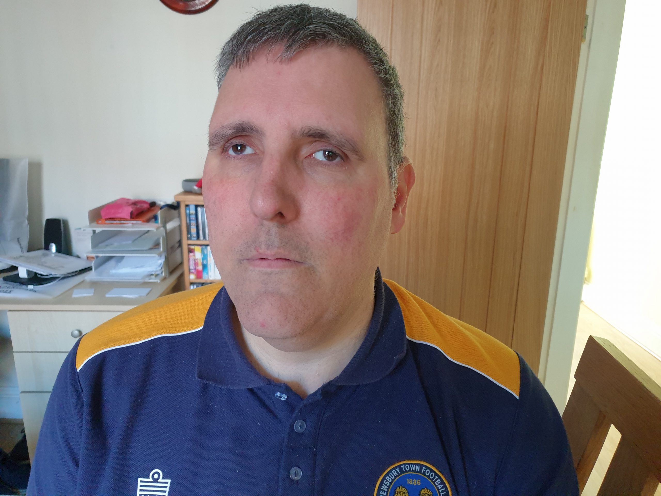 Richard Zimbler headshot. Richard has grey hair and is wearing a navy blue and yellow football polo shirt. He is smiling at the camera.
