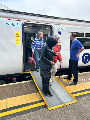 Try a Train attendee getting off a train using a ramp, assisted by a sighted guide.