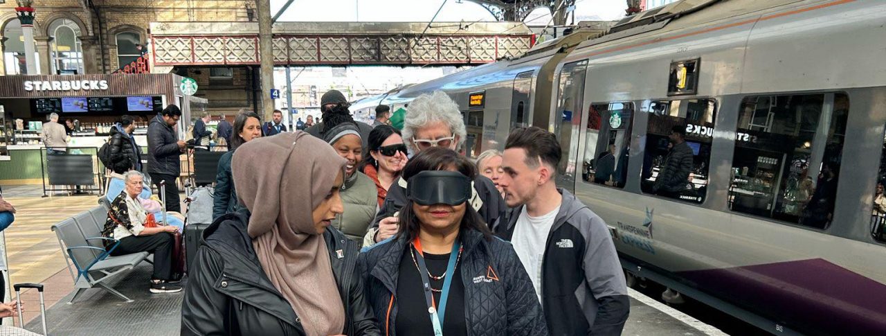 Six people standing on a railway platform at Preston train station, including members of Avanti West Coast and Community Rail Lancashire. A smartly dressed lady standing at the front of the group is wearing black sim specs.