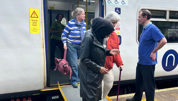 Try a Train attendee getting off a train using a ramp, assisted by a sighted guide.