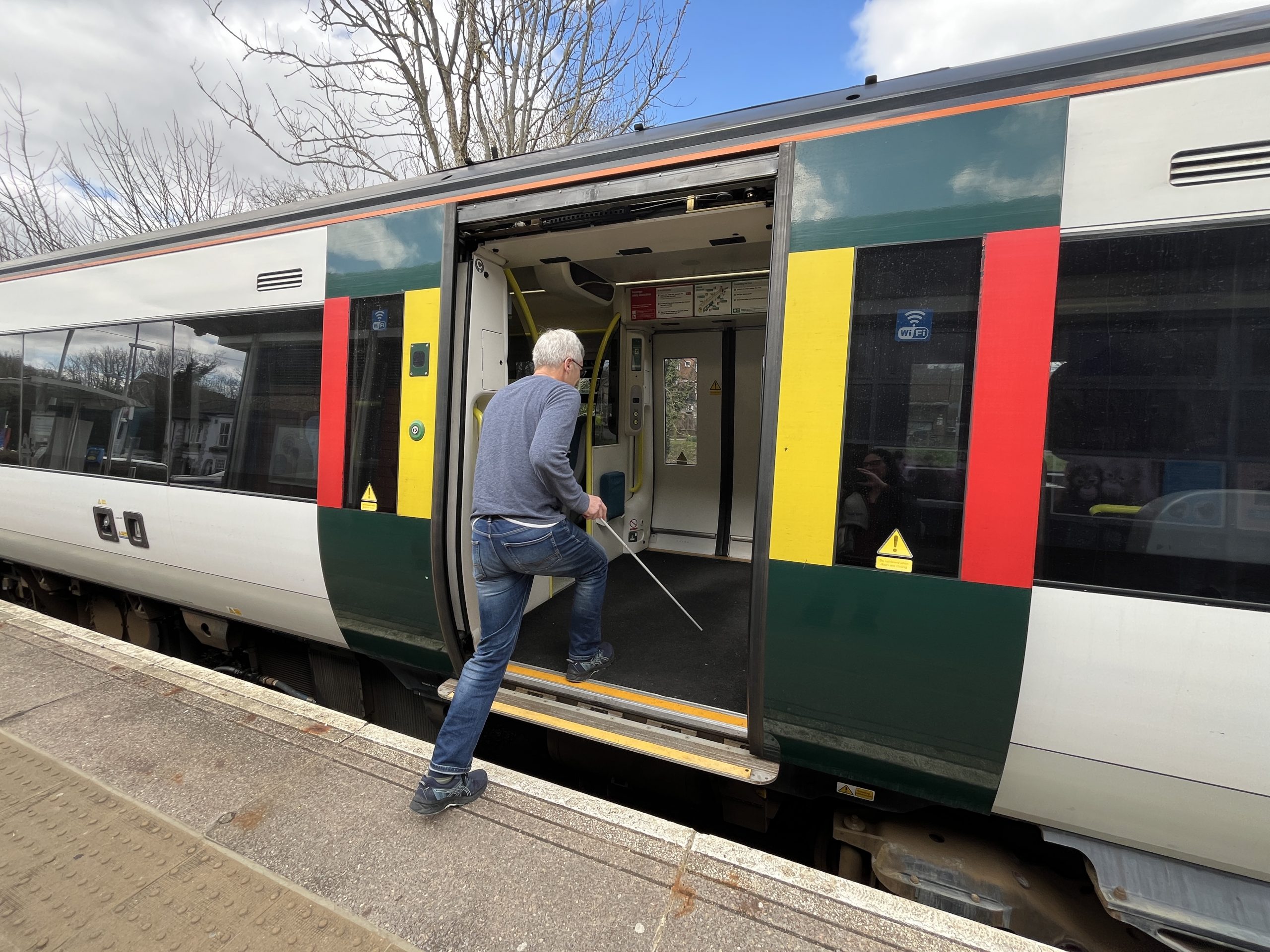 SLC volunteer Clinton is boarding a train. He is holding his navigation cane.