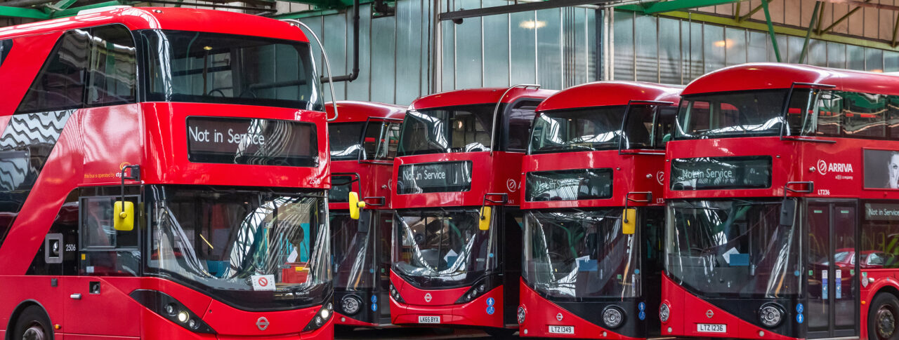 Row of four red double-decker buses parked in a line.