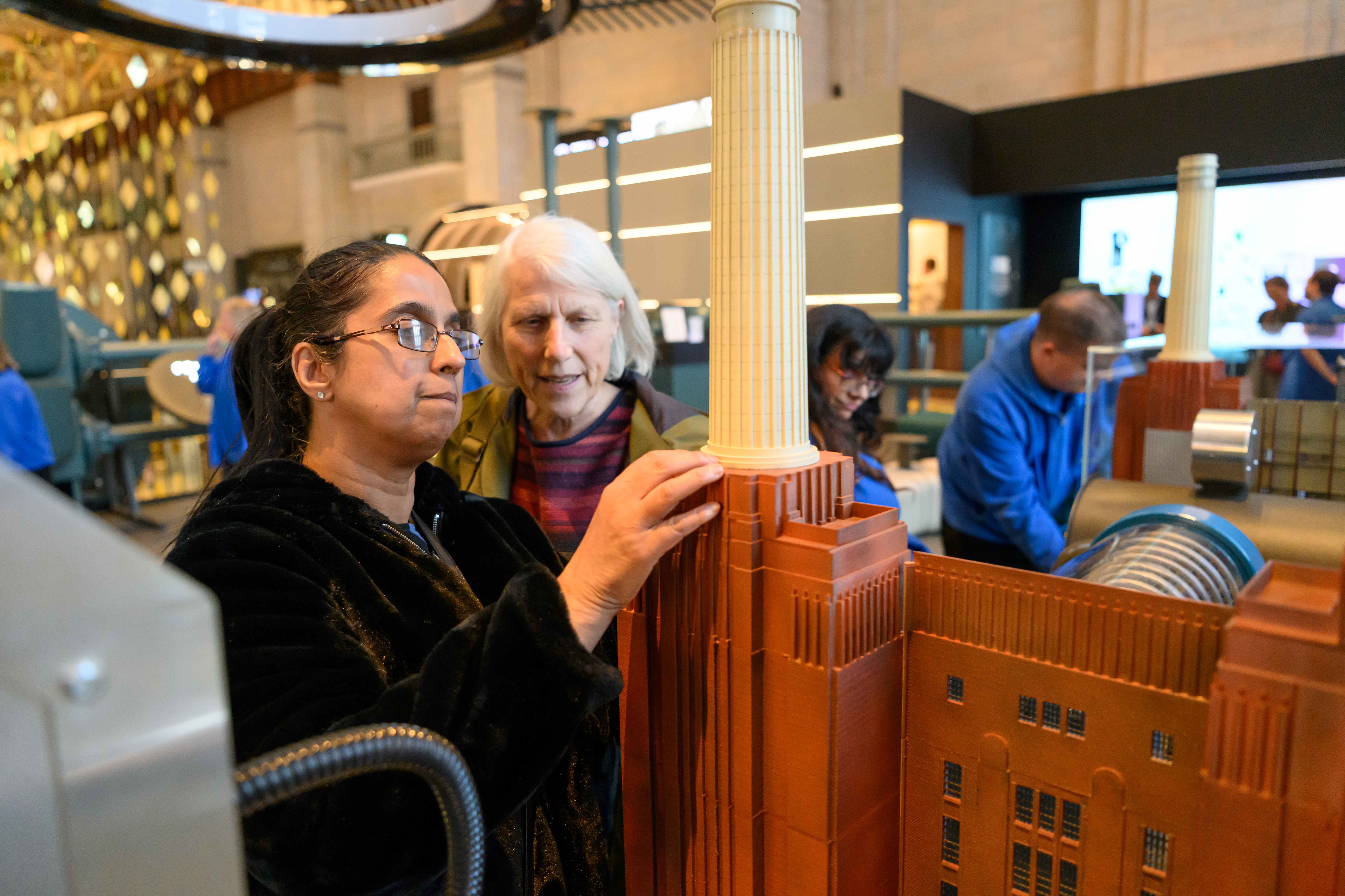Amrit, North London SLC member, is stood in front of a large scale model of Battersea Power Station. She is feeling the structure of the two chimneys, with her support worker looking on.