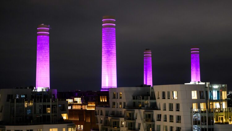 Arial photo of Battersea Power Station at night, with it's four chimneys lit up in purple.