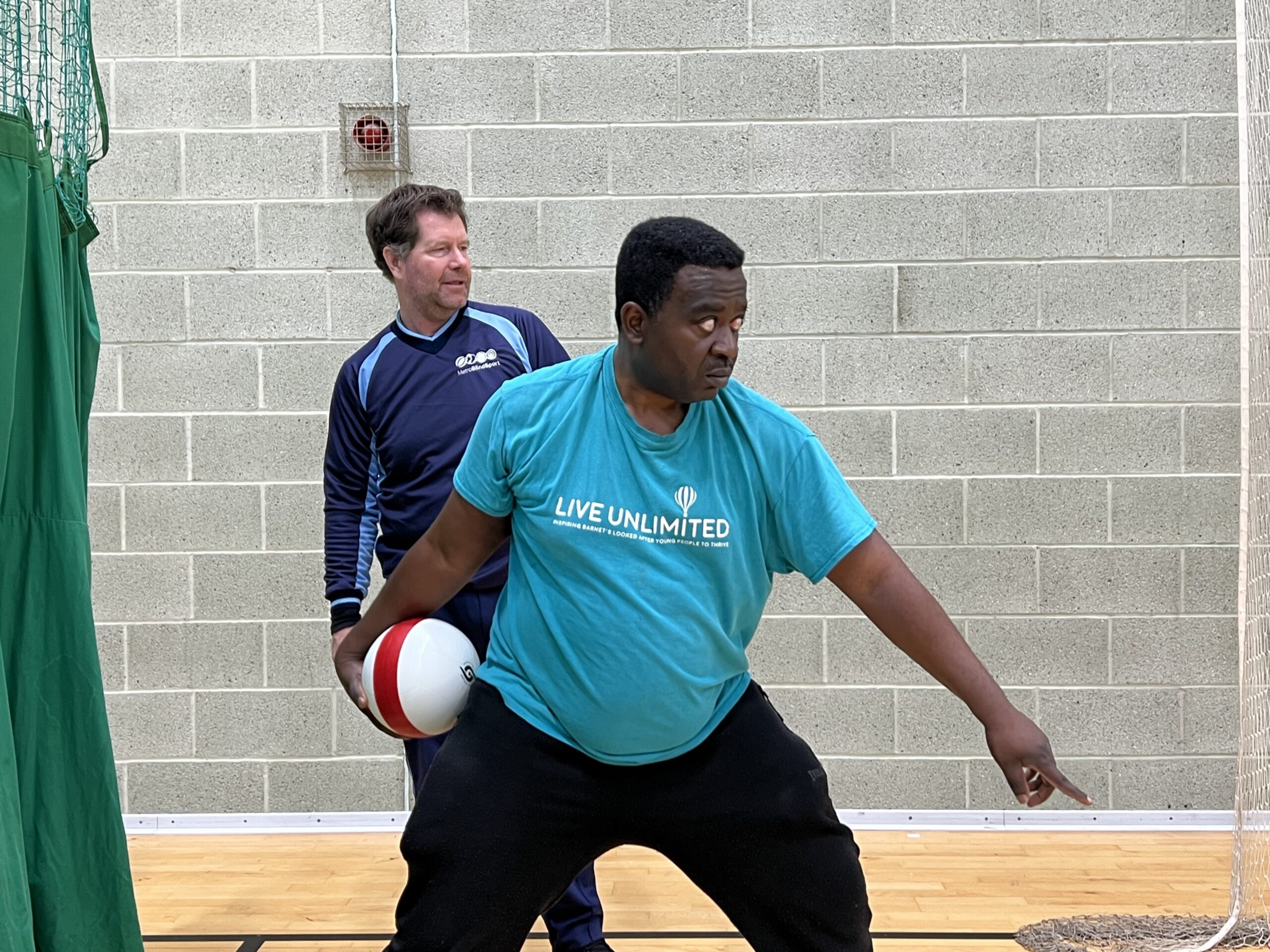 Mo, a male attendee is pictured practising bowling techniques with Rory Field standing behind him, during one of the VI Cricket sessions. He has a look of intense concentration on his face.