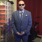 Photo of Carl Galloway, Birmingham and B=lack Country SLC member. Carl is wearing a blue/grey checked suit and pale blue tie, sunglasses, and smiling at the camera.