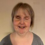 Headshot of Nottinghamshire SLC member, Kay Dear. She is standing against a cream wall, smiling at the camera.