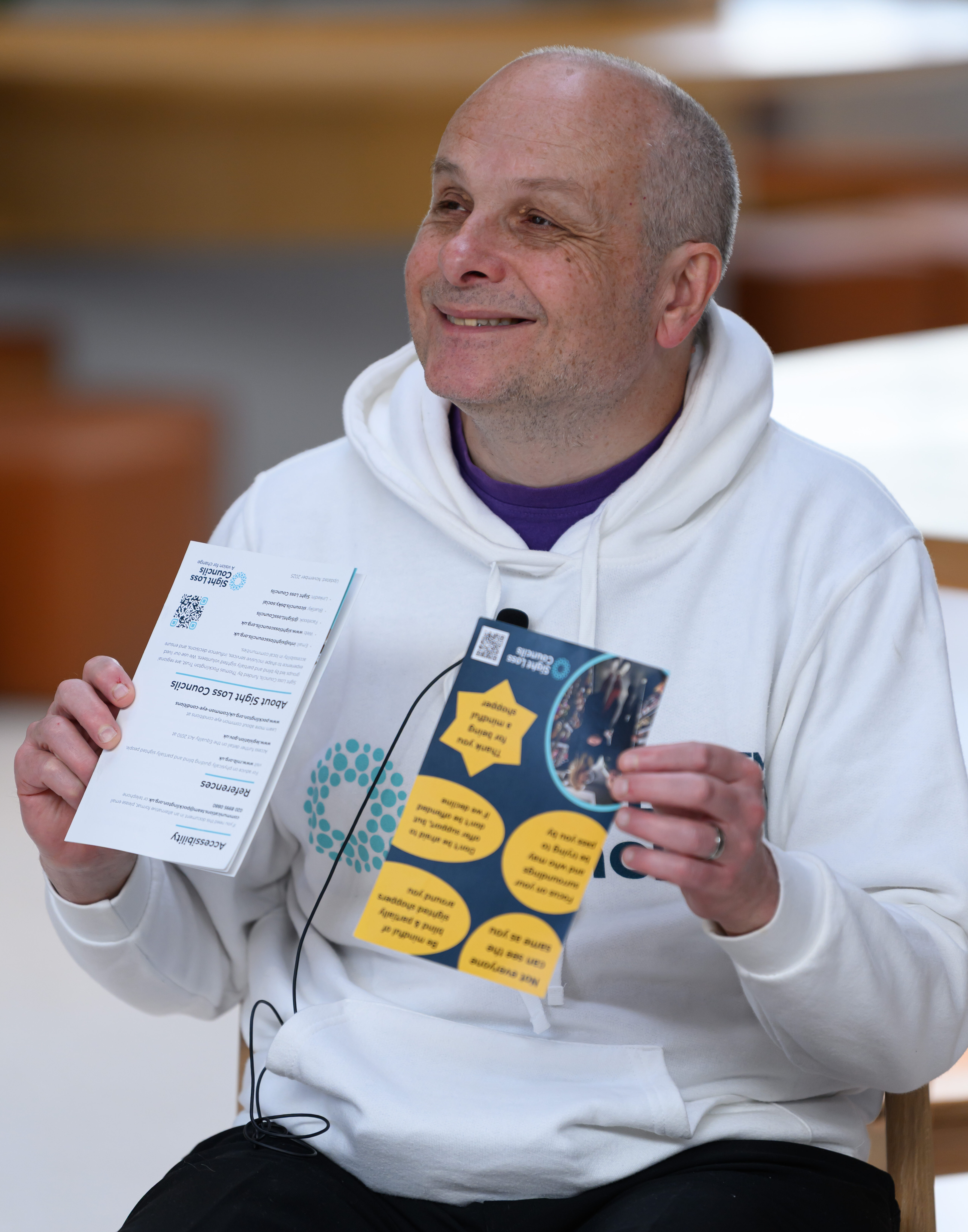 Liam O'Carroll, Interim Engagement Manager for London SLCs, is sat smiling, holding up our 'Mindful Shopper' poster, on an access panel discussion.