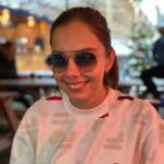 Head shot of Zehra, Sussex SLC member. Zehra is is wearing sunglasses and has her hair scraped back into a ponytail. She is wearing a white, long sleeved top, and is smiling in the direction of the camera.