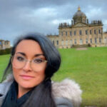 Selfie style photos of Vicky thompson, SLC Coordinator for Yorkshire and Humberside. She has long, dark hair and is wearing glassed. She is stood outside on a lawn, in front of a historical building. The sky is black.