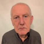 Headshot of David Quarmby, West Yorkshire SLC member. He is wearing a dark shirt and stood against a cream wall. He is looking at the camera.