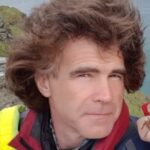 Photo of Mike Winder, Derbyshire Sight Loss Council member. He is wearing outdoor, hiking clothing, and is on top of a hill. He has dark brown hair, which is windswept.