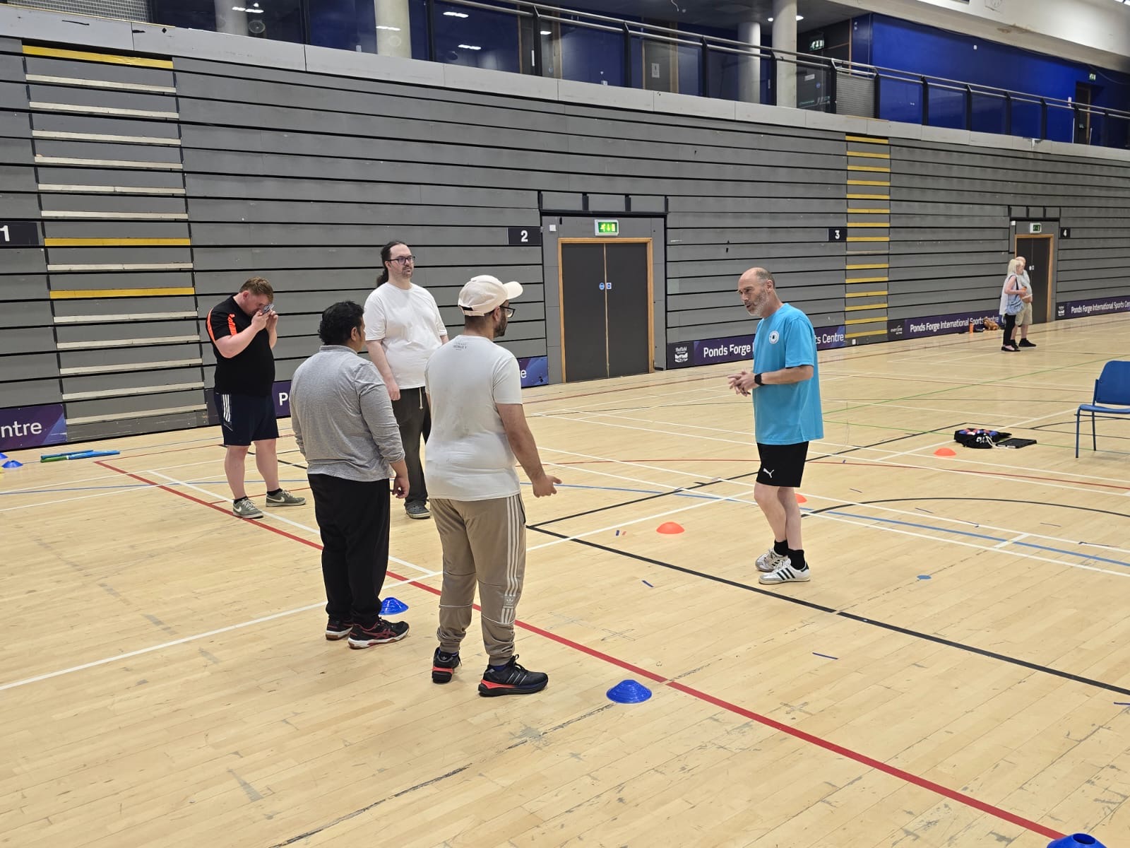 a group of four BPS people in a gym hall, facing an instructor who is delivering a session during South Yorkshire SLCs Let's Get Active Day. There are raised markers laid out on the floor around them.